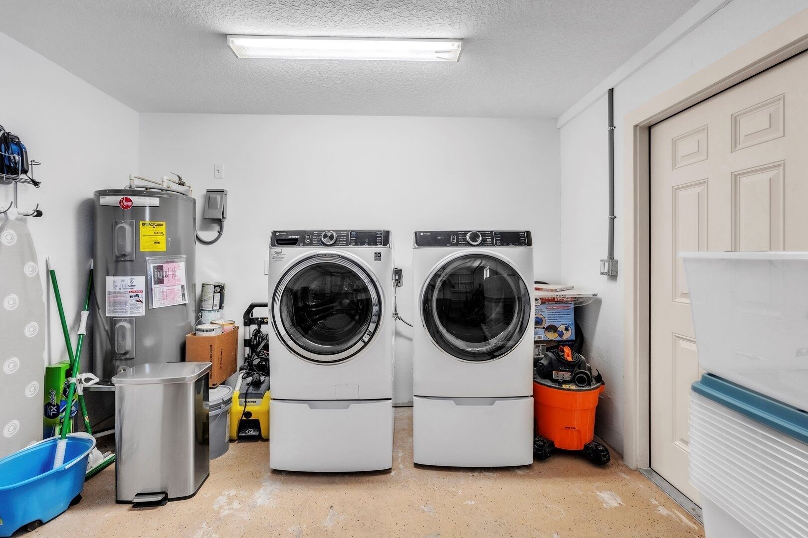 A laundry room with two front-loading washing machines, a metal utility sink, and a blue bucket.