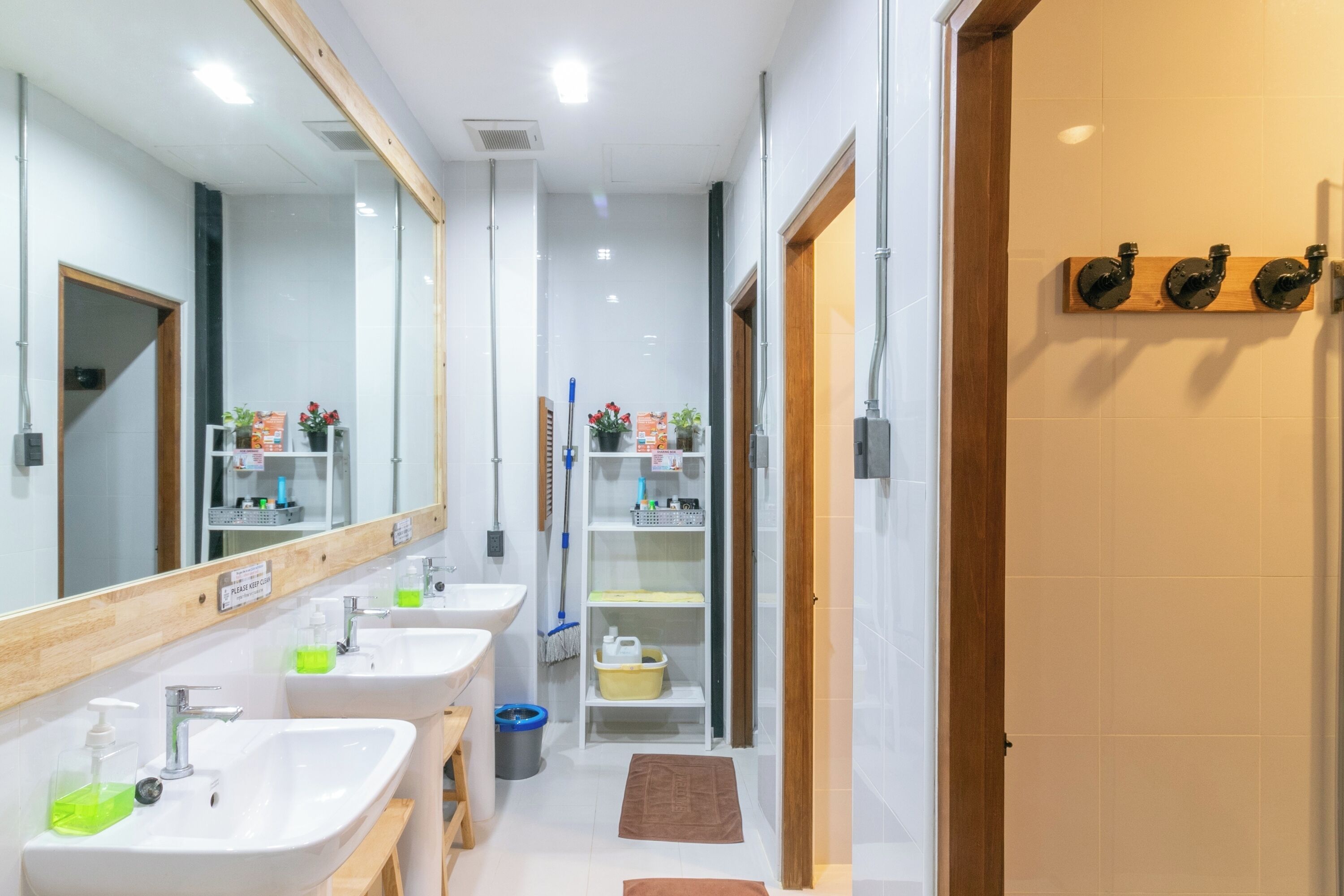 Un bagno moderno con tre lavabi, uno specchio grande e uno scaffale in legno con asciugamani.