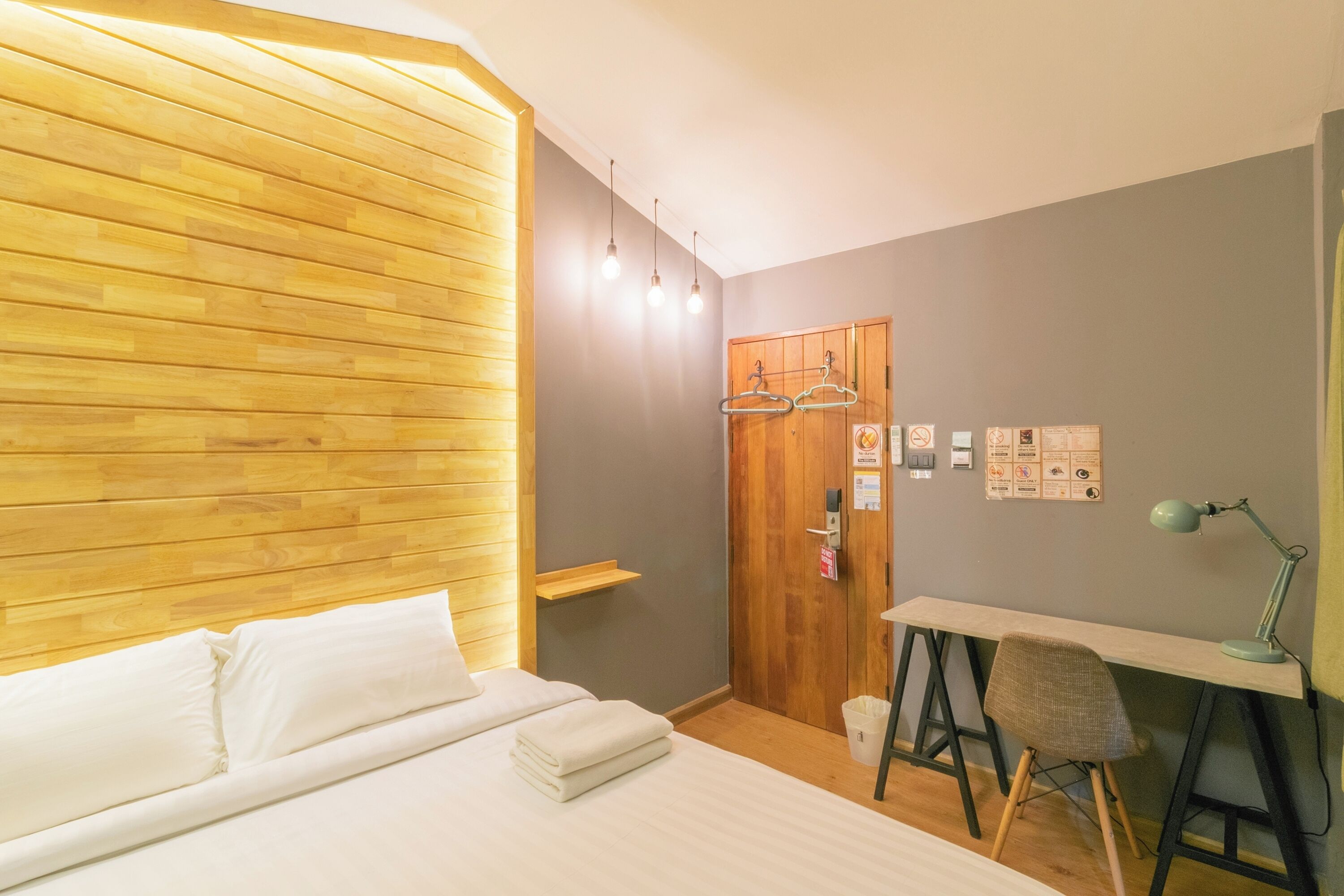 A hotel room with a wooden headboard, a bed with white linens, a desk with a chair, and a hanging light fixture.