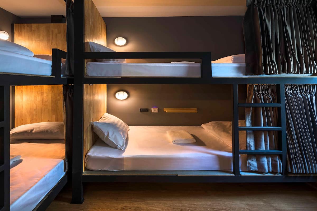 A bunk bed room with a wooden floor, a ladder, and a circular light fixture on the wall.