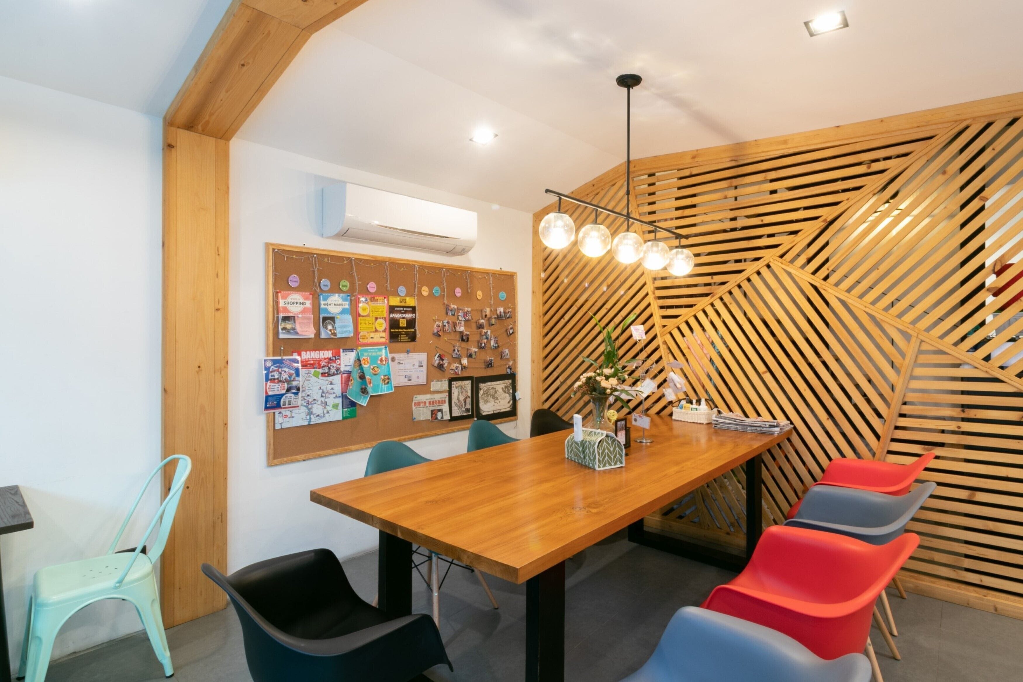 A modern meeting room with a wooden table, colorful chairs, a bulletin board, and a unique wooden slat wall design.