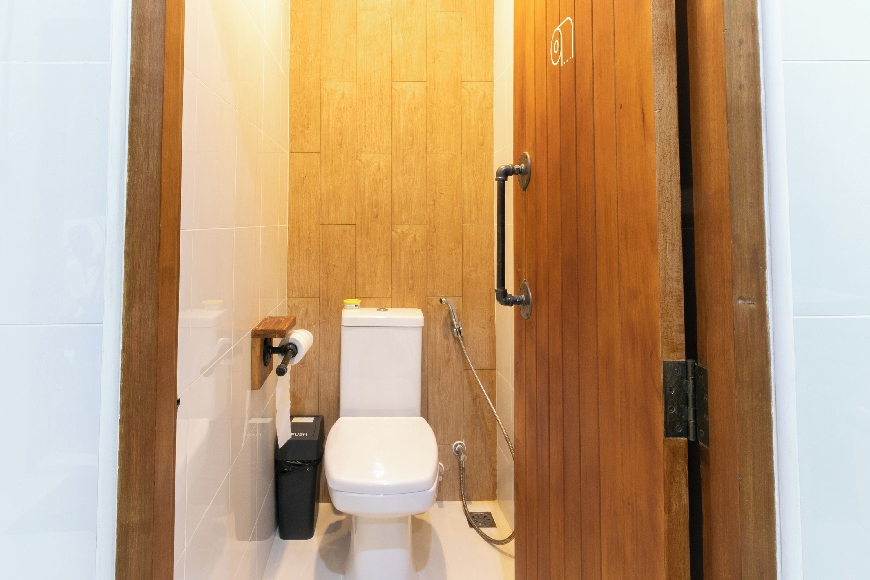 Puerta de madera que da a un baño con inodoro, ducha y secamanos.