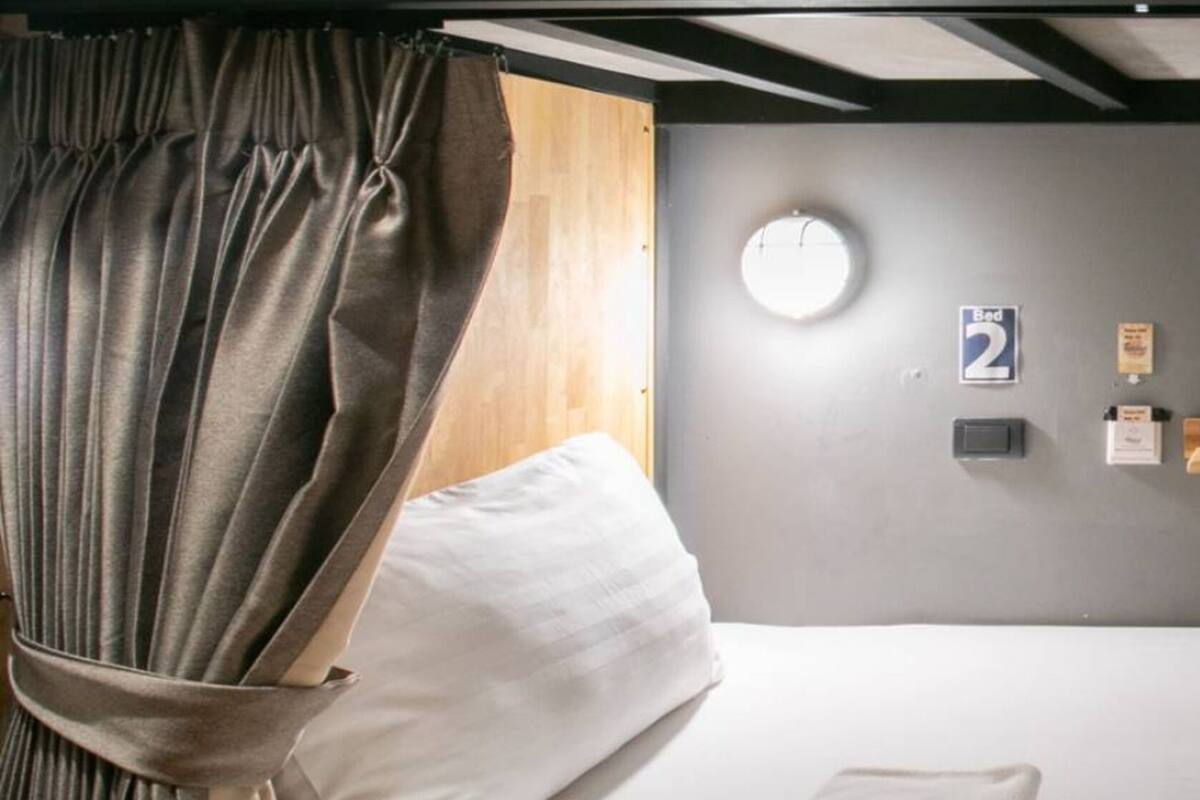 A single-bed room with a curtain, a bedside table, a wall clock, and a bed number sign.