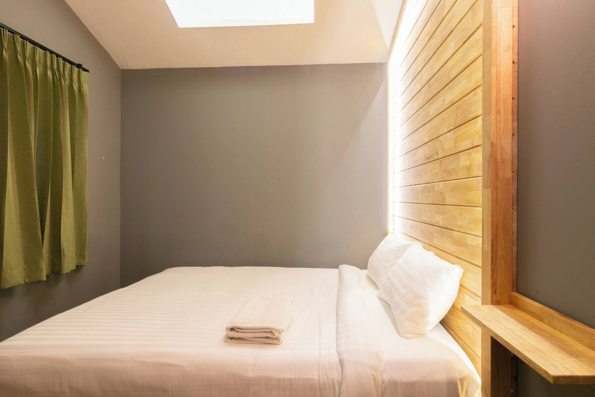 A neatly made bed with a folded towel, a wooden headboard, and a skylight above.