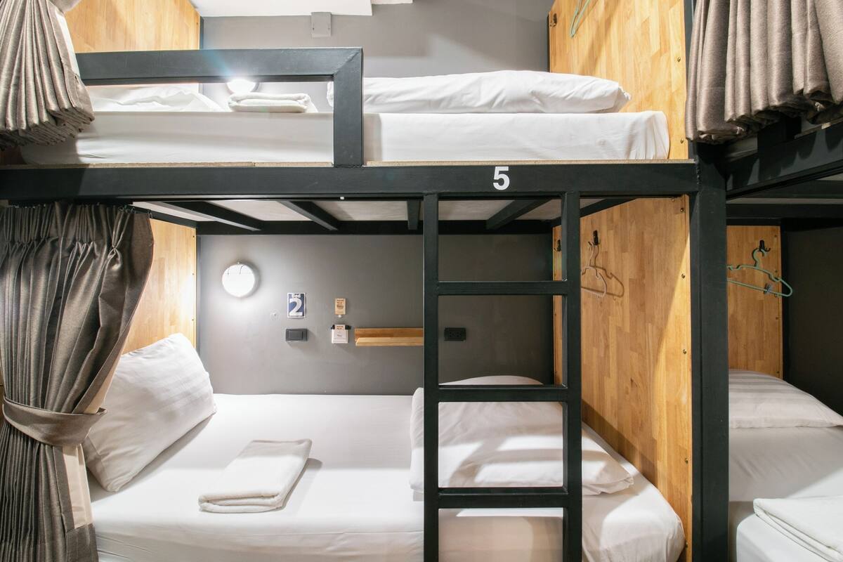 A bunk bed room with a wooden headboard, a number '5' on the top bunk, a clock on the wall, and a towel on the lower bunk.