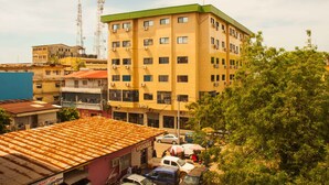 A multi-story building with a green roof, surrounded by parked cars and trees. - L'Almamya Hôtel & Résidence (Conakry)