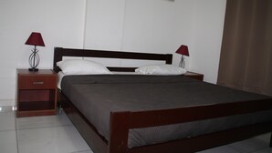 A neatly made bed with a wooden headboard, two bedside tables with lamps, and a white tiled floor. - L'Almamya Hôtel & Résidence (Conakry)