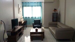 A living room with a TV, a coffee table, a sofa, and a dining table. - L'Almamya Hôtel & Résidence (Conakry)
