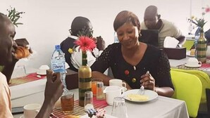 A group of people seated around a table with various items like a bottle, a glass, and a plate of food. - L'Almamya Hôtel & Résidence (Conakry)