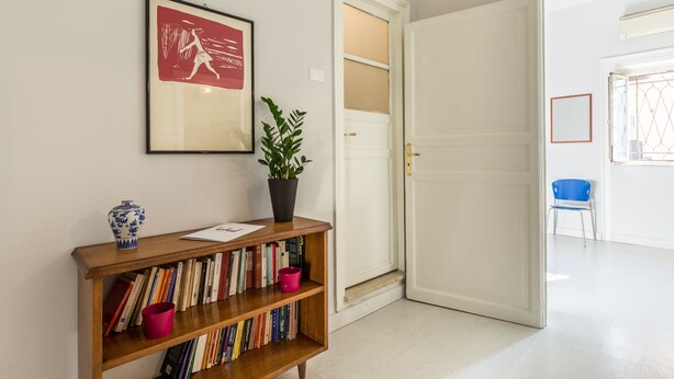 A hallway with a bookshelf, a framed picture, a potted plant, and a door leading to another room. - Casa Dante with Balcony by Wonderful Italy (Palermo)