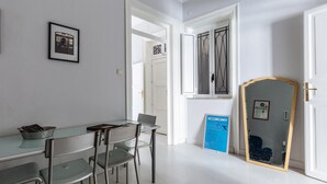 A room with a glass table, metal chairs, a framed picture, a door with a metal gate, and a blue informational sign. - Casa Dante with Balcony by Wonderful Italy (Palermo)