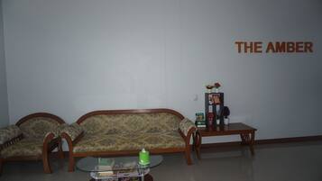 Sala de estar com sofá, duas poltronas, uma mesa de centro e uma mesinha lateral. Na parede, uma placa com a inscrição "THE AMBER".