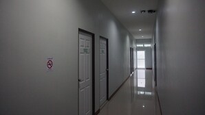 A long, narrow hallway with doors numbered 102 and 103, and a no-smoking sign on the wall. - The Amber Mansion (Roi Et)