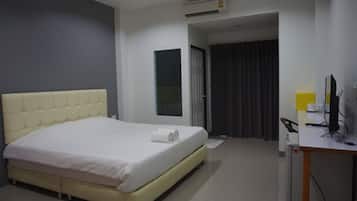 A hotel room with a bed, a desk, a chair, an air conditioner, and a window with curtains.