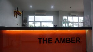 A reception desk with "THE AMBER" signage, air conditioning units, and a view of the outside through large windows. - The Amber Mansion (Roi Et)