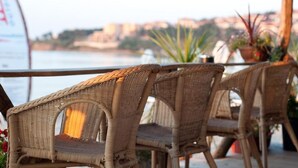 Wicker chairs on a terrace with a view of the sea and buildings in the background. - Blue Orange Beach Resort (Sozopol)