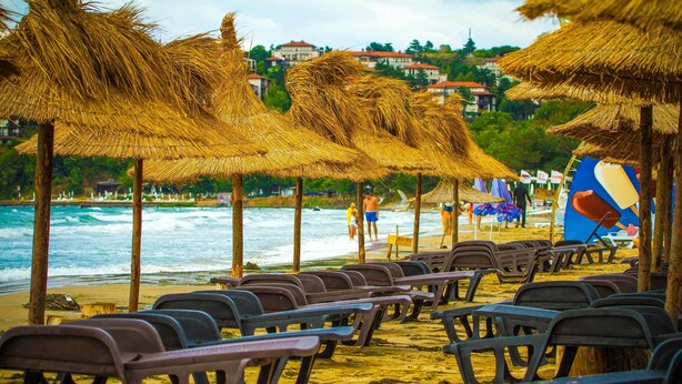 A beach with rows of plastic chairs under thatched umbrellas, a sandy shore, and the ocean in the background. - Blue Orange Beach Resort (Sozopol)