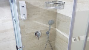 A modern shower with a handheld showerhead and a wall-mounted faucet, a soap dispenser, and a metal shelf. - Hostal Bahía (Cádiz)