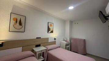 Quarto de hotel com duas camas, uma escrivaninha, uma cadeira e obras de arte nas paredes.