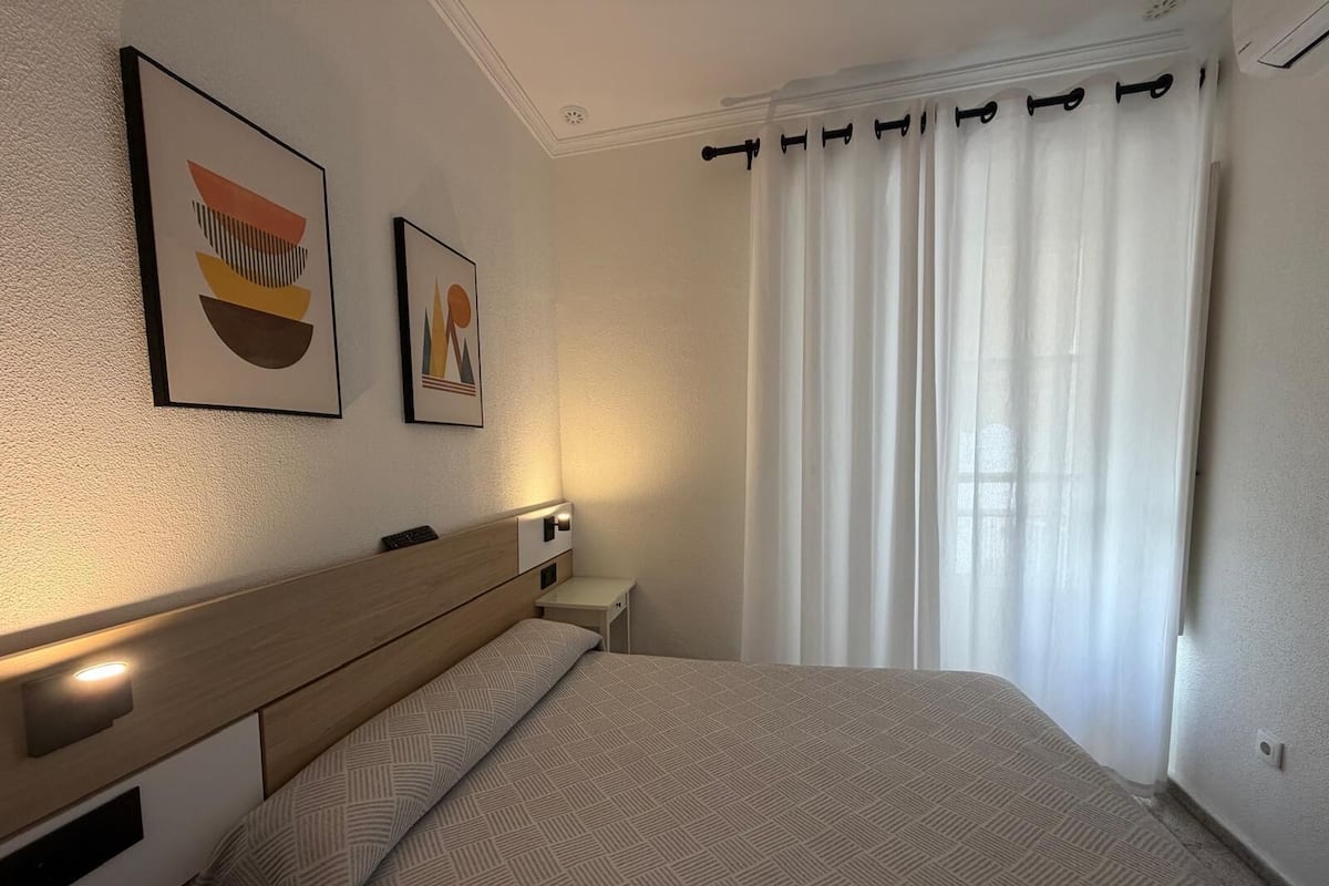 A neatly arranged hotel room with a bed, a bedside table, a wall-mounted lamp, and two framed artworks.