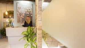 Zona de recepción con una recepcionista, un cuadro grande en la pared y plantas en macetas.