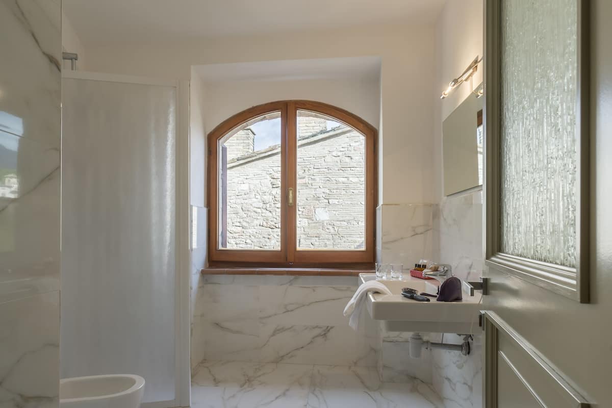 A bathroom with a marble floor, a window with a stone wall view, a sink, and a toilet.
