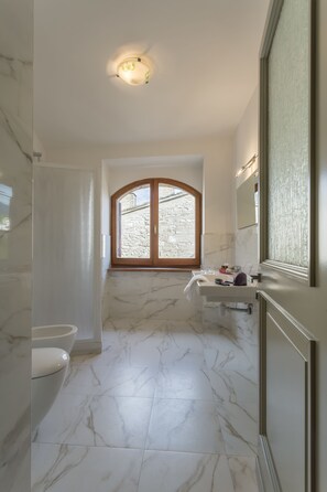 A bathroom with a marble floor, a window with a stone wall view, a sink, and a toilet. - Hotel Il Duomo (Assisi)