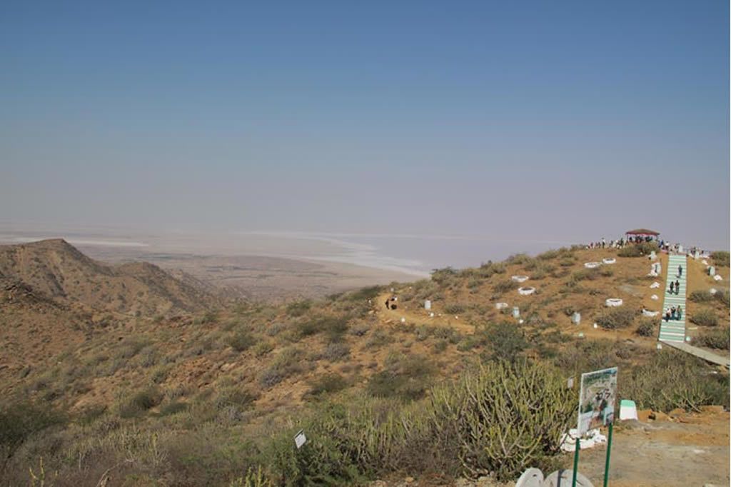 A desert landscape with a building on a hill, a pathway, and scattered graves.