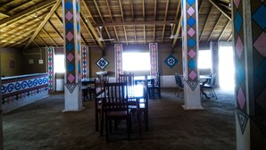 Un vaste espace intérieur doté de hauts plafonds et de poutres en bois, comprenant un espace de détente central avec des tables et des chaises, ainsi que des murs aux motifs décoratifs.