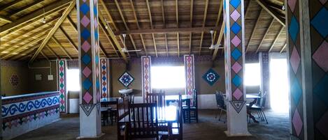 A spacious indoor area with high ceilings and wooden beams, featuring a central seating area with tables and chairs, and patterned walls.