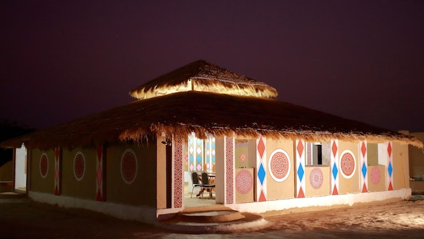 Un bâtiment à toit de chaume, orné de motifs géométriques colorés sur les murs, avec une porte centrale et une petite fenêtre.