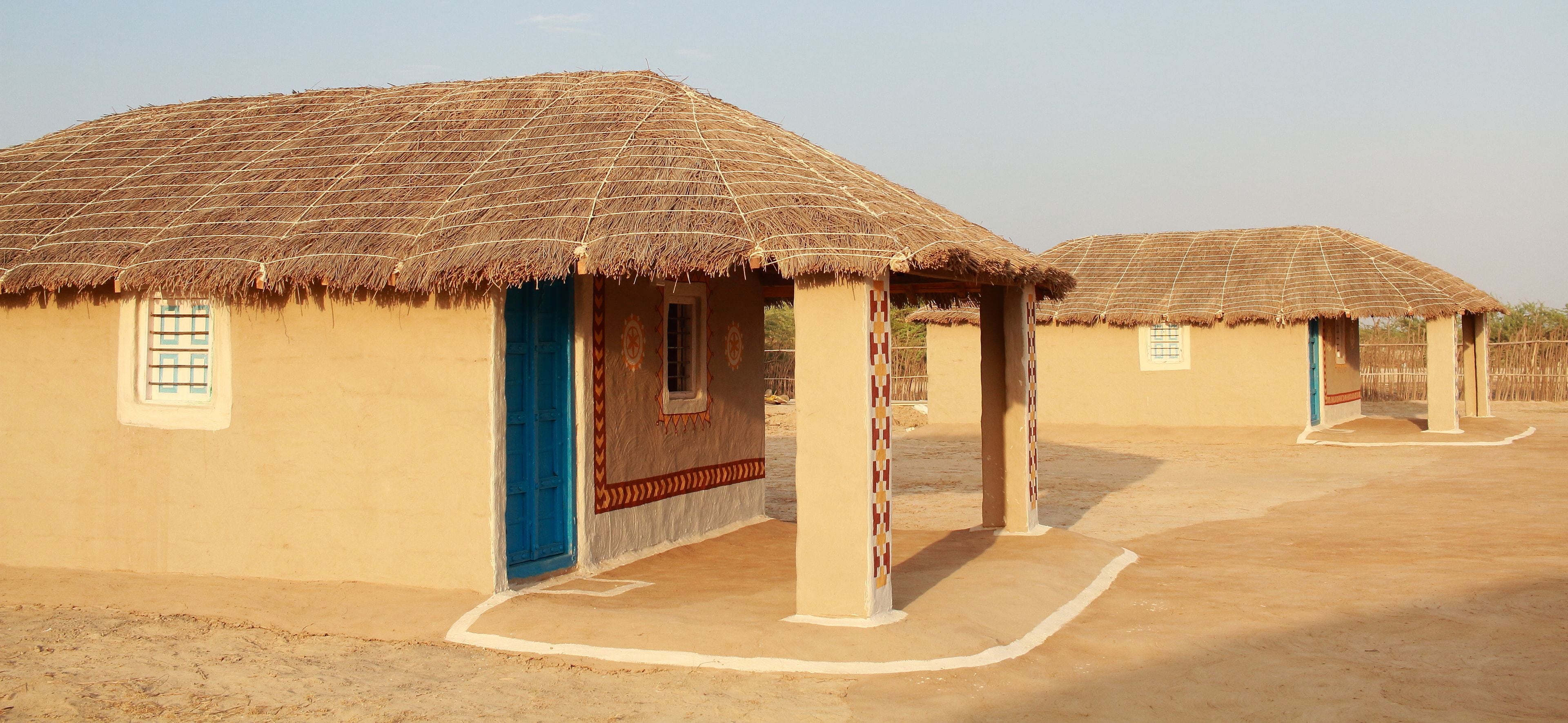 A row of thatched-roof huts with a simple, open design, featuring a central door and windows, and a flat, unadorned ground.