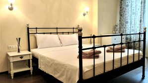 A bedroom with a black metal bed frame, white bedding, a bedside table with a lamp, and a nightstand with a vase of flowers. - Baratero City Corner Apartment (Sofia)