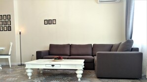 A living room with a brown sofa, a white coffee table, patterned floor tiles, and a white chair. - Baratero City Corner Apartment (Sofia)