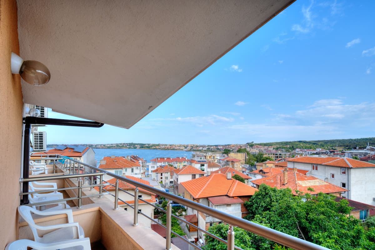 A balcony with a view of a coastal town, railings, and a clear sky.