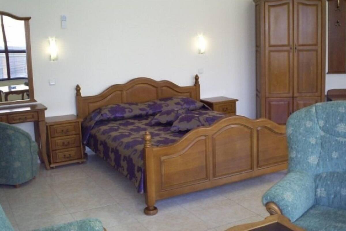 Ein Schlafzimmer mit einem hölzernen Bett, einem Nachttisch, einer Kommode, einem Stuhl und einem Spiegel.