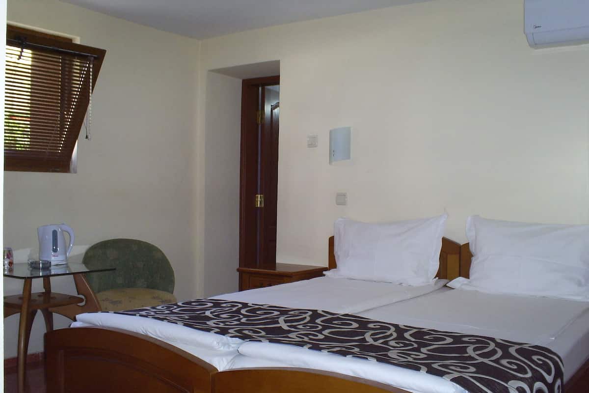 Ein Hotelzimmer mit einem hölzernen Bett, einem kleinen Tisch mit Wasserkocher, einem Sessel und einem Fenster mit Jalousien.