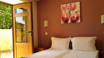 Ein Hotelzimmer mit einem Bett, einem Blumenbild an der Wand, einem Fenster mit Blick auf Grünflächen und einer Tür.