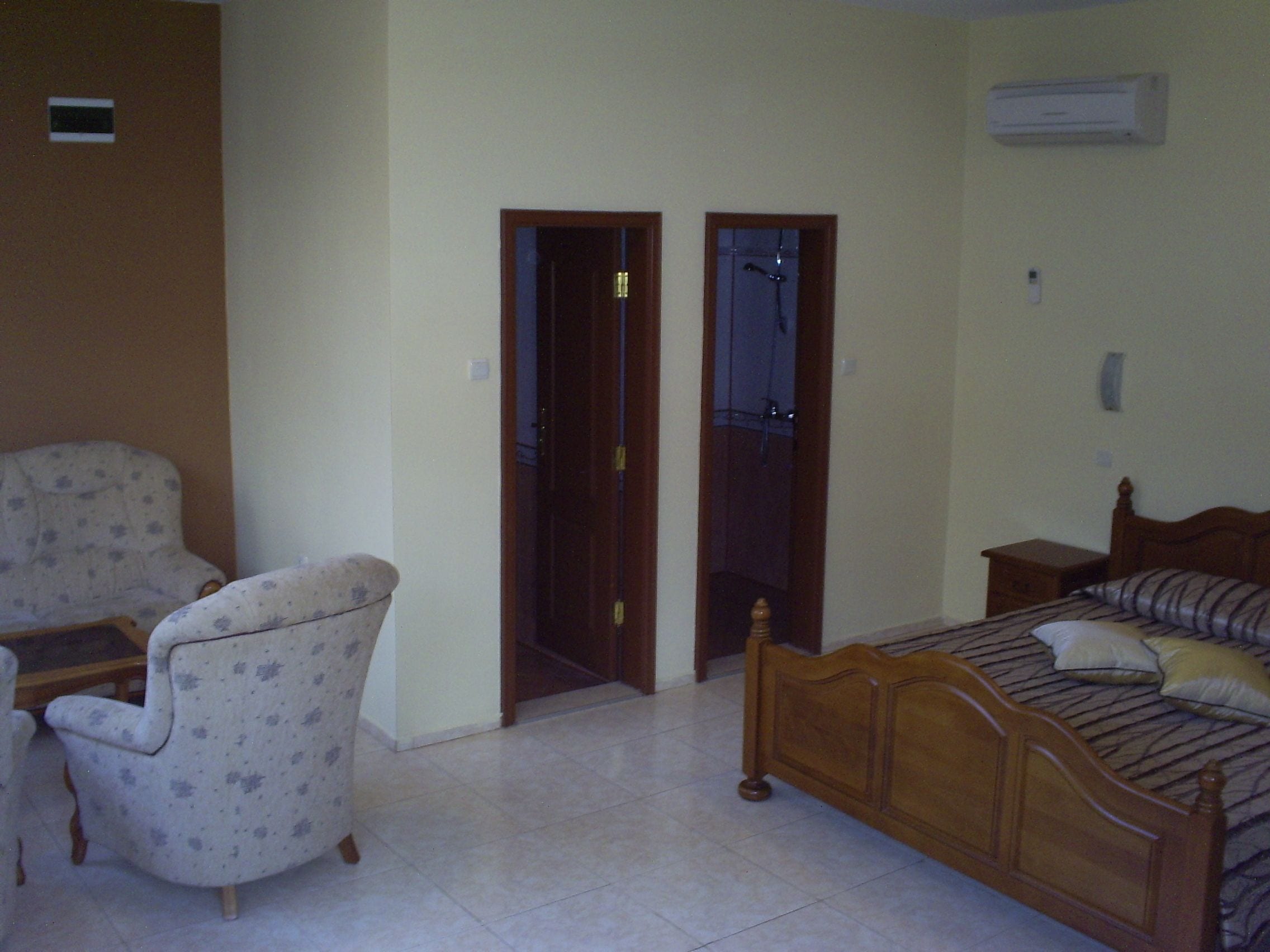 A bedroom with a bed, a chair, a wooden wardrobe, and a door leading to another room.