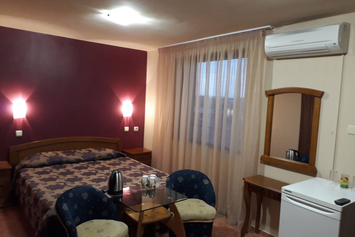 Ein Hotelzimmer mit einem Bett, zwei Nachttischen, einem Glastisch mit Stühlen, einer Klimaanlage und einem Spiegel.