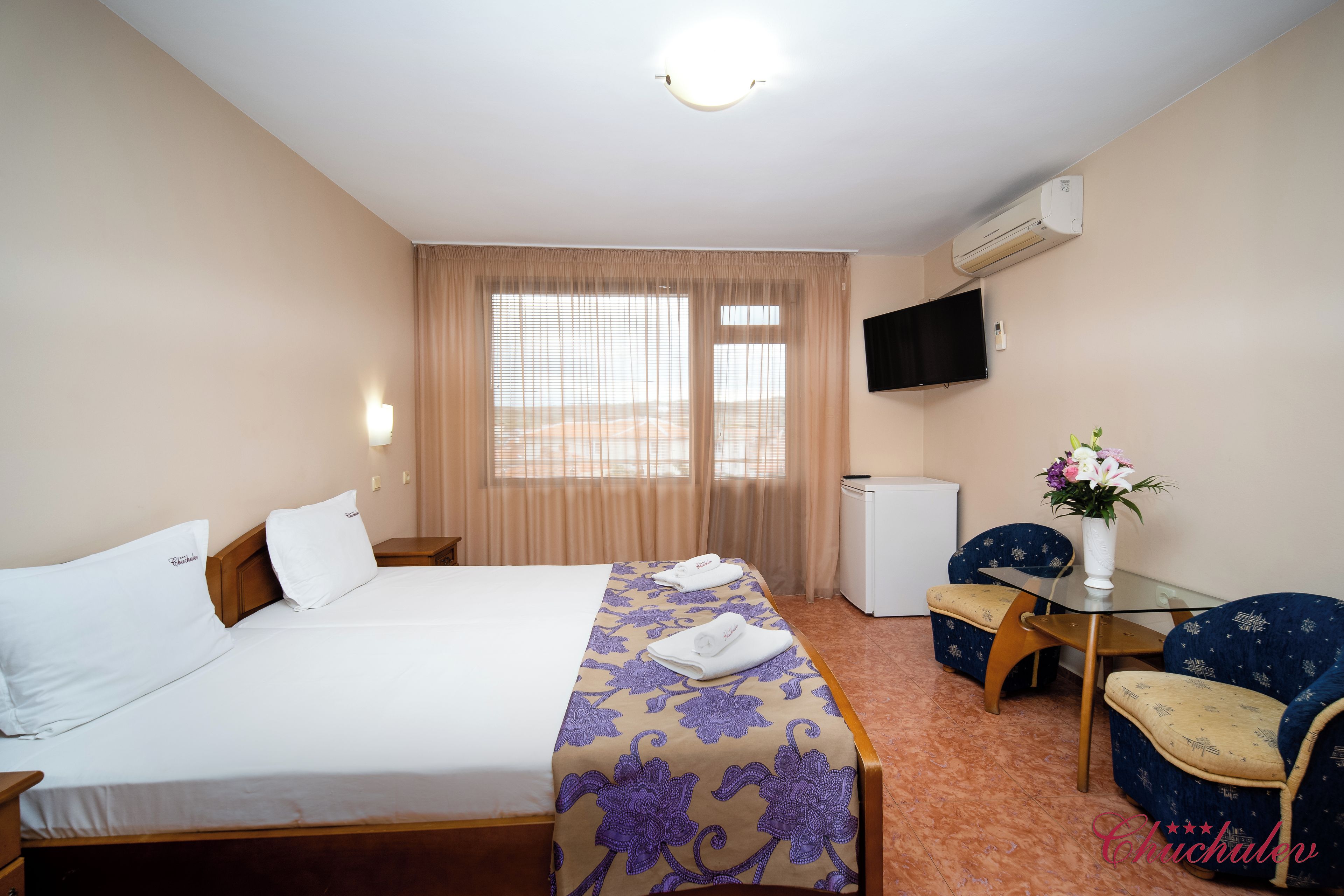 A hotel room with a bed, a desk, a chair, a TV, and an air conditioner.