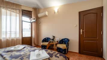 Una habitación de hotel con una cama, dos sillas, una mesita con una tetera y una puerta.