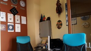 A room with two blue office chairs, a desk with a computer, a telephone, and various certificates on the wall.