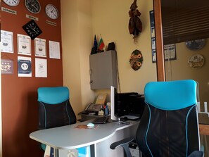 A room with two blue office chairs, a desk with a computer, a telephone, and various certificates on the wall.