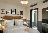 A hotel room with a bed, bedside lamps, framed pictures on the wall, a mirror, and a door leading to a bathroom.