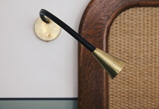 A modern lamp with a black handle and brass accents, mounted on a wall with a woven texture.