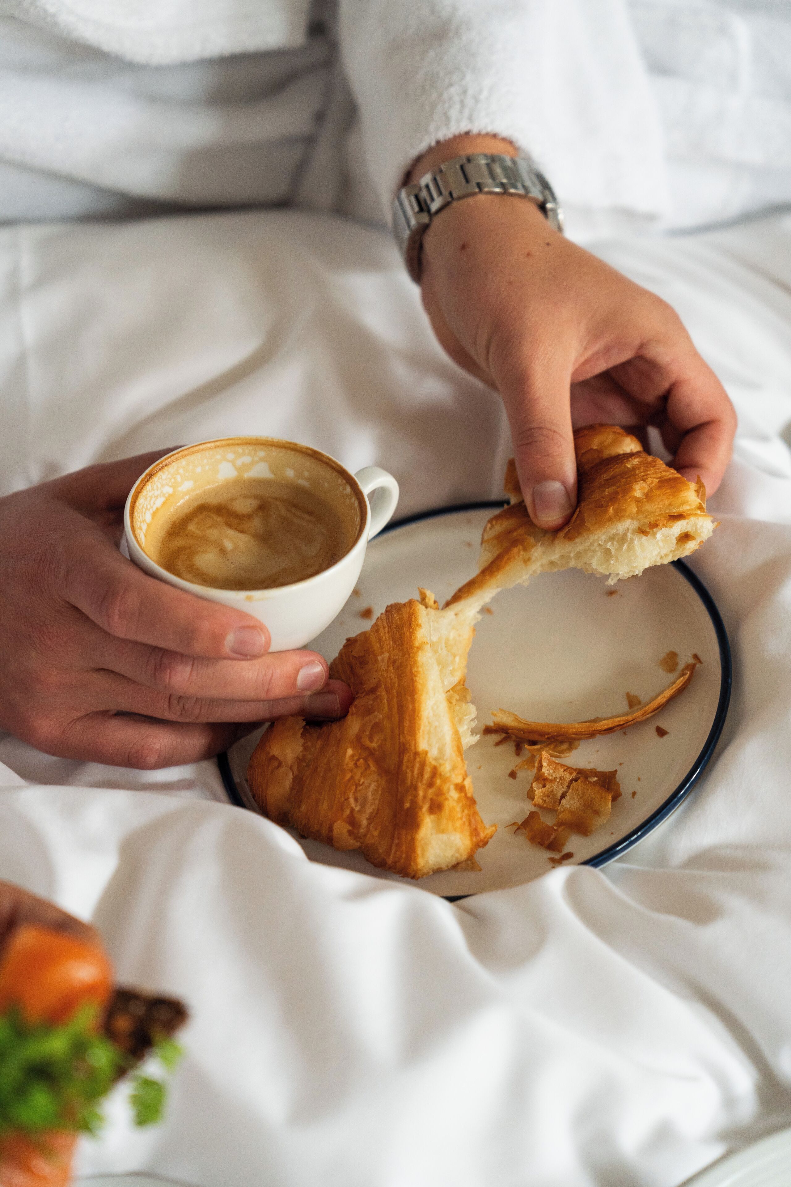 A person holding a cup of coffee and a piece of bread on a plate.