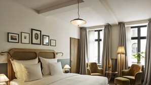 A hotel room with a large bed, a sitting area with two chairs, a side table, a lamp, and a window with curtains. - Hotel Sanders (Copenhagen)