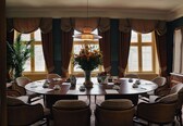 A dining room with a round table, chairs, a vase of flowers, and curtains.