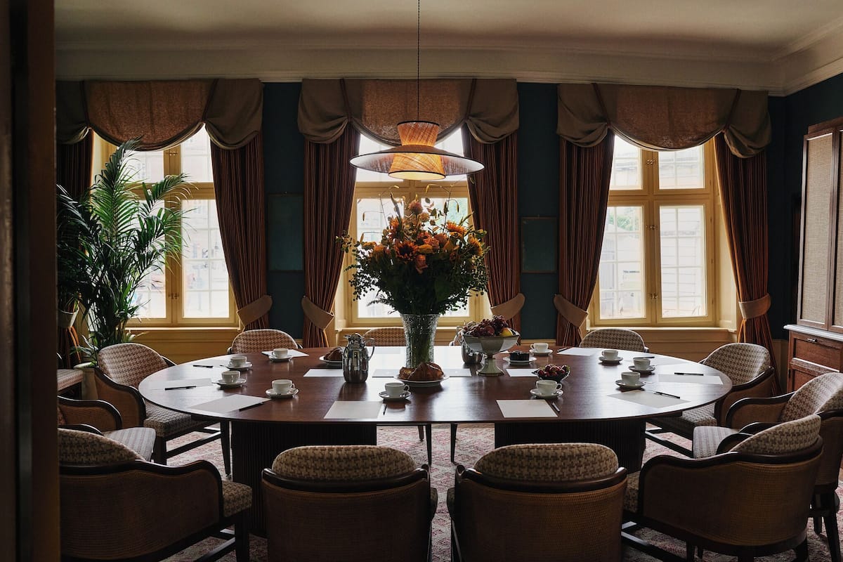 Comedor con una mesa redonda, sillas, un jarrón de flores y cortinas.